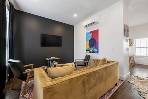 A living room with a sofa, chairs, a flat-screen TV, and a colorful painting on the wall. - Stylish 2BR -  W&D - Downtown Location (Bentonville)