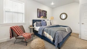 A bedroom with a bed, a chair, a bedside table, a lamp, a mirror, and a window with blinds. - Stylish 2BR -  W&D - Downtown Location (Bentonville)