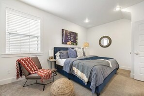 Une chambre à coucher comprenant un lit, une chaise, une table de chevet, une lampe, un miroir et une fenêtre avec des stores.
