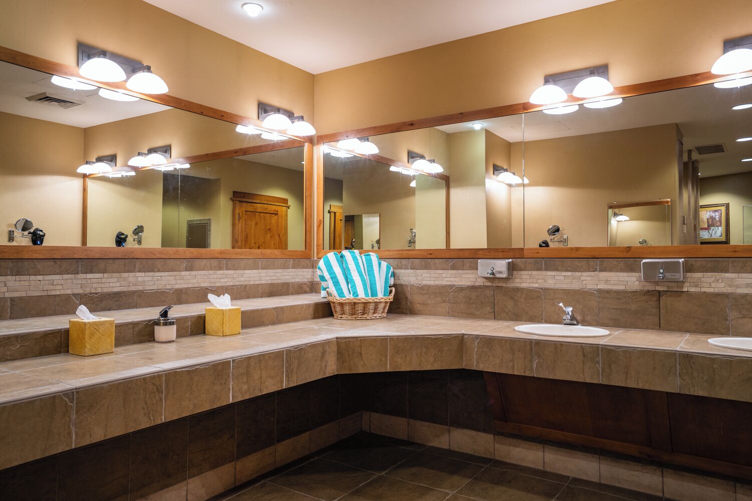 Baño público con varios lavamanos, espejos y un mueble de tocador de madera.