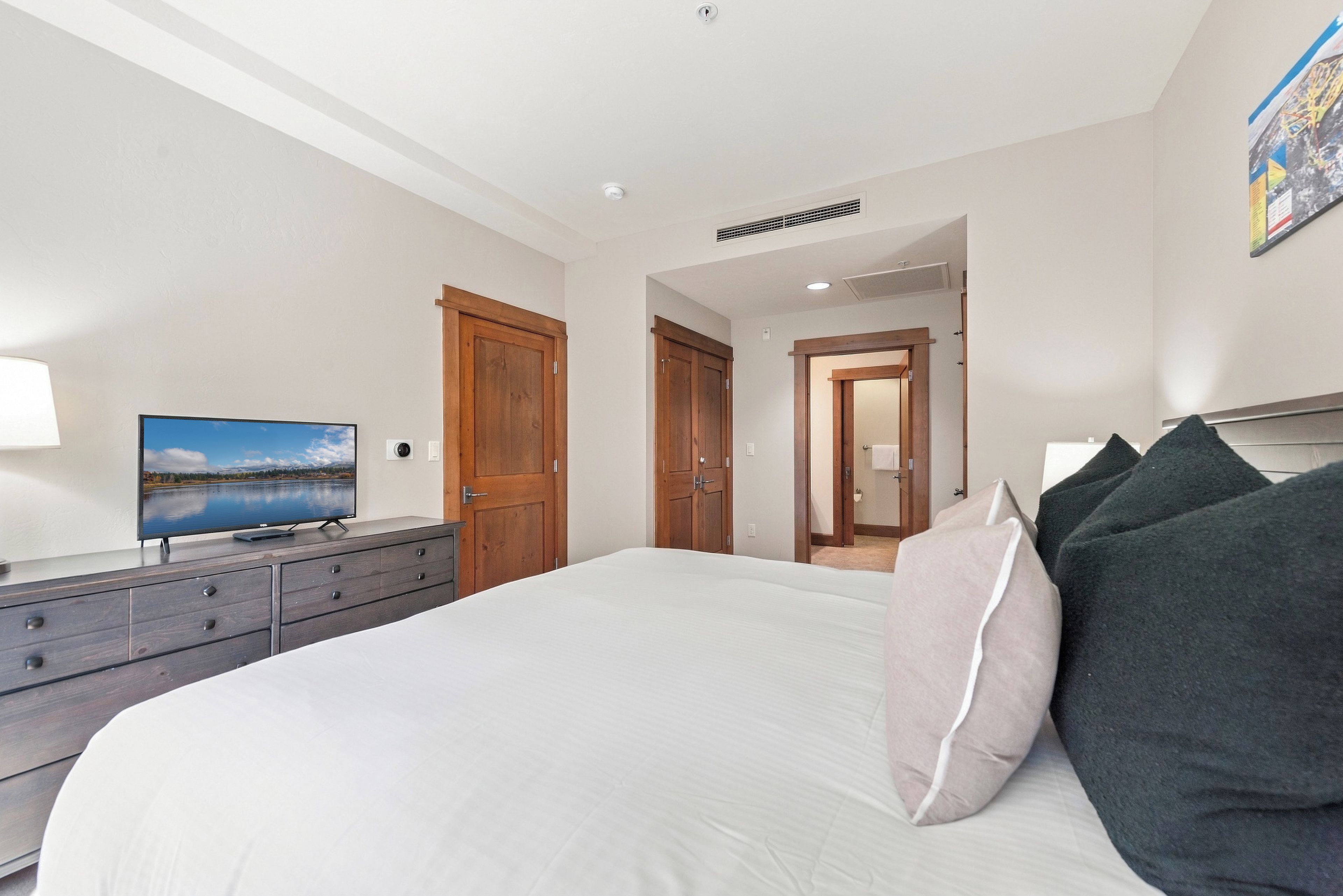 A bedroom with a bed, a dresser, a television, and a door leading to another room.