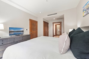Una camera da letto con un letto, una cassettiera, una televisione e una porta che dà su un'altra stanza.