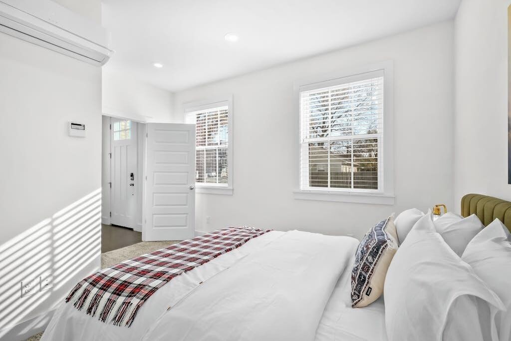 Un dormitorio con cama, ventana con persianas, puerta y un termostato en la pared.