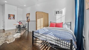 Une chambre à coucher moderne avec un cadre de lit en métal, une literie à rayures, un tapis à motifs léopard et un petit coin repas comprenant une table et des chaises.