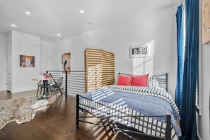 Una camera da letto moderna con un letto a struttura in metallo, biancheria a righe, un tappeto a stampa leopardo e un piccolo angolo ristoro con tavolo e sedie.