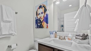 Une salle de bain moderne avec un lavabo blanc, des meubles en bois foncé, un grand miroir et un tableau accroché au mur.