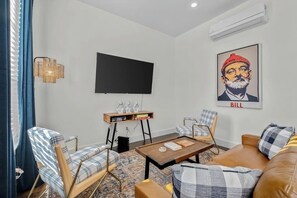 Una sala de estar moderna con un televisor de pantalla plana, un sofá, dos sillones, una mesa de centro y una estantería.