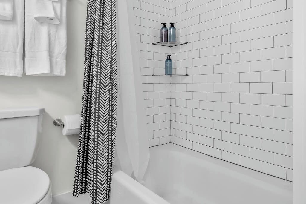 Ein Badezimmer mit weiß gefliester Wand, einer Toilette, einem Duschbereich und einem waschbärigen Duschvorhang.