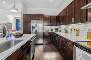 Una cocina moderna con armarios de madera oscura, electrodomésticos de acero inoxidable y encimera blanca.