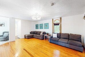 A spacious living room with hardwood flooring, a sectional sofa, a small table, and a decorative wall with three framed pictures. - 7BR Lakefront Dog Friendly - Private Pool (Garfield)