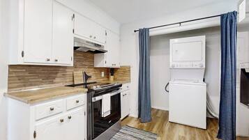 A compact kitchen with white cabinets, a built-in oven, a microwave, and a washing machine.