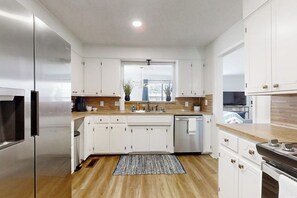 Cocina moderna con armarios blancos, electrodomésticos de acero inoxidable y encimera de madera.