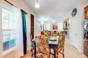 A dining area with a table set for four, surrounded by patterned chairs, a chandelier, and a view of the outdoors.