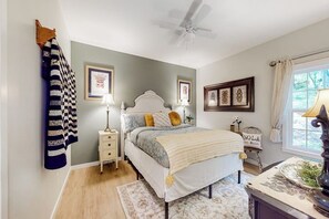 A bedroom with a bed, bedside tables, a ceiling fan, and artwork on the walls.