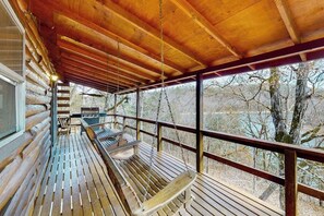 Eine Holzterrasse mit Schaukel, Bank und Tisch, mit Blick auf einen bewaldeten Bereich.