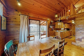 Eine Holzhütte mit Essbereich, Küche und einer Treppe, die zu einer oberen Ebene führt.