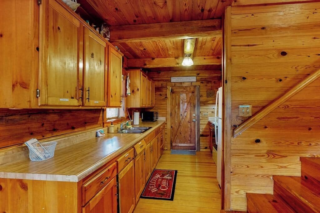 Een houten chalet van binnen met een keuken, houten kastjes, een magnetron en een trap.