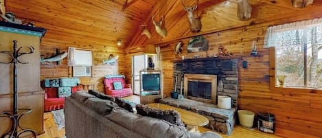 L’intérieur d’un chalet rustique, avec une cheminée en pierre, un plafond en bois et des têtes de cerf accrochées au mur.