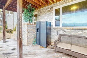 A covered outdoor area with a brick wall, a black refrigerator, a wicker sofa, and a window with a view. - 5BR Spacious Lakefront Home with Game Room (Hot Springs)