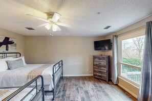 A bedroom with a bed, a ceiling fan, a dresser, a television, and a window with curtains. - 5BR Spacious Lakefront Home with Game Room (Hot Springs)