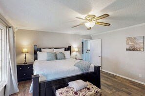 Ein Schlafzimmer mit Bett, Nachttischen, Deckenventilator, einer Bank und einer Tür.