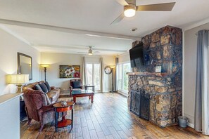 A living room with a stone fireplace, a ceiling fan, and a sofa with multiple cushions. - 5BR Spacious Lakefront Home with Game Room (Hot Springs)