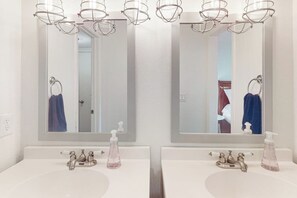 Une salle de bain avec deux lavabos, chacun étant surmonté d’un miroir. On trouve deux distributeurs de savon sur les lavabos.