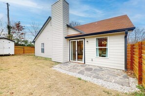 A single-story house with a stone patio, a garage, and a wooden fence. - OZK Trail House | Downtown, Bikes & Dogs (Bentonville)