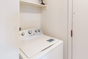 A white wall-mounted washer and dryer unit with control knobs, a vent, and a small shelf above it. - OZK Trail House | Downtown, Bikes & Dogs (Bentonville)