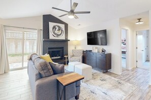 Ein geräumiges Wohnzimmer mit Kamin, Deckenventilator, Flachbildfernseher und großem Fenster.