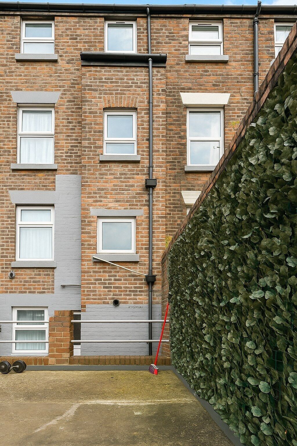 Ein Backsteinhaus mit mehreren Fenstern, einem Metallzaun und einer Hecke.