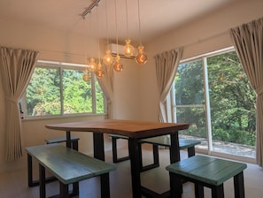 A dining area with a wooden table and benches, large windows with curtains, and hanging light fixtures. - Minamiizu Shimoda/OpalNest/ArtHouse/10p/PetsOK/New (賀茂郡南伊豆町)