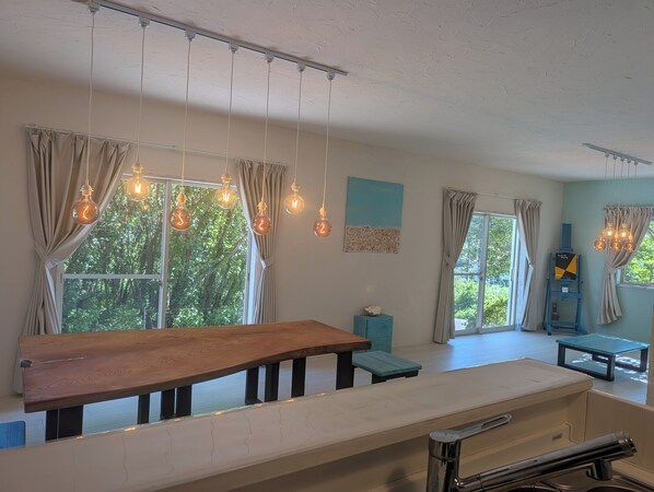 Habitació amb taula de fusta, lluminàries penjants i vista a la vegetació.