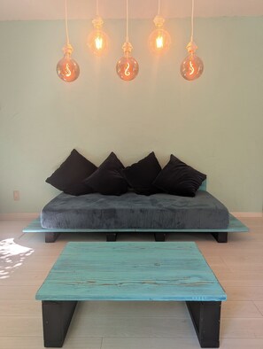 A room with a sofa, pillows, a table, and hanging light bulbs.