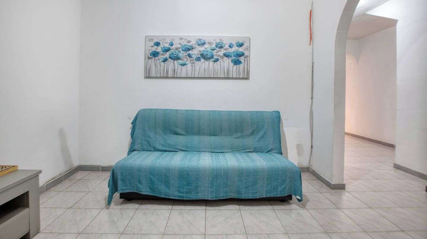 Una stanza con un divano verde acqua, un quadro appeso al muro e un pavimento piastrellato.