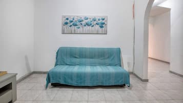 Una stanza con un divano verde acqua, un quadro appeso al muro e un pavimento piastrellato.