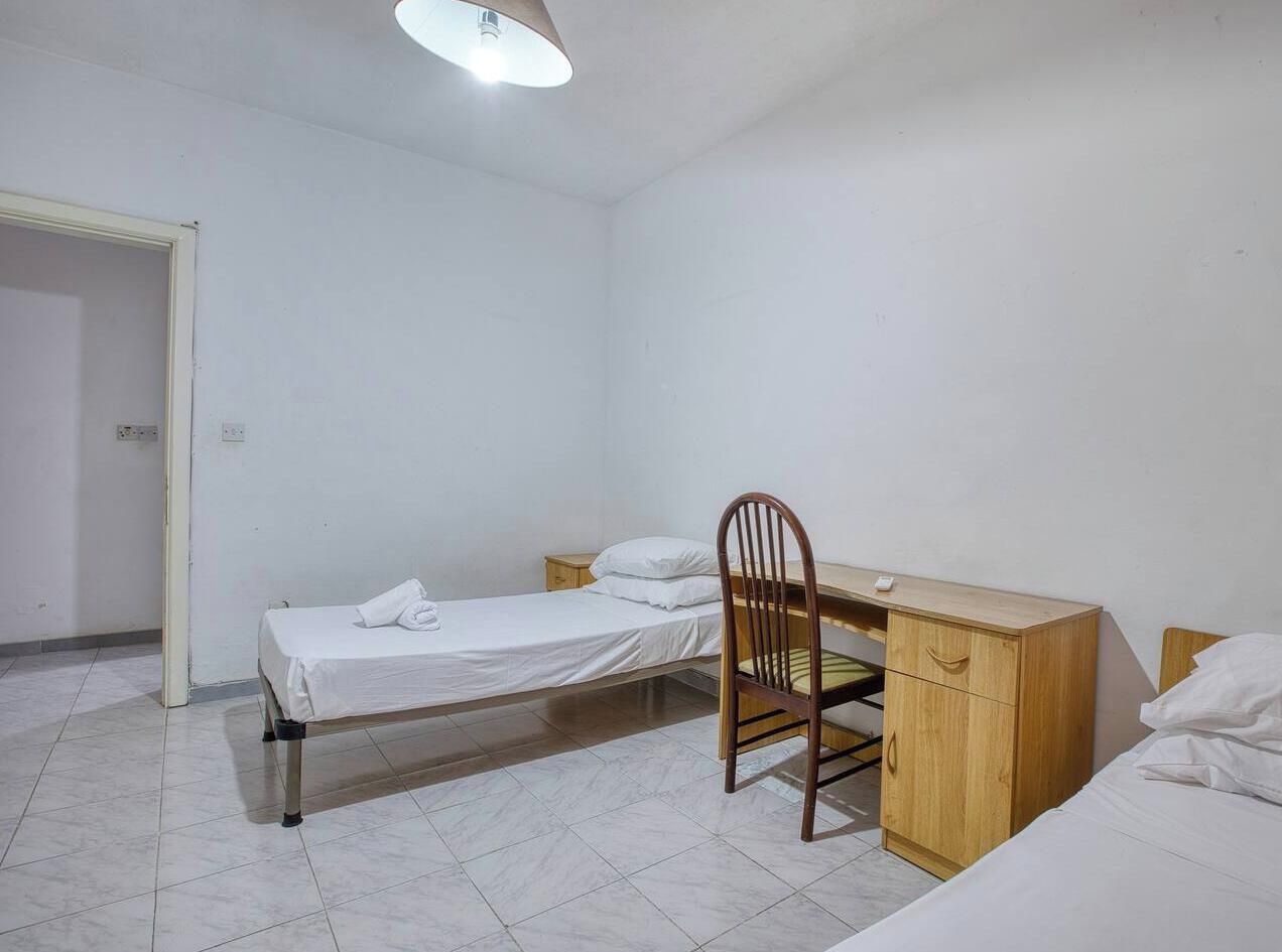 Ein kleines, sauberes Zimmer mit einem Einzelbett, einem Holztisch und einem Stuhl.
