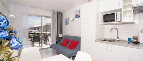 A modern hotel room with a balcony, a kitchenette, and a dining area.