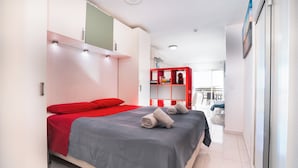 A modern hotel room with a bed, a red wardrobe, and a view of the outside.