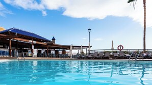 A swimming pool with lounge chairs and umbrellas, a covered area with a blue roof, and a lifebuoy on the deck.
