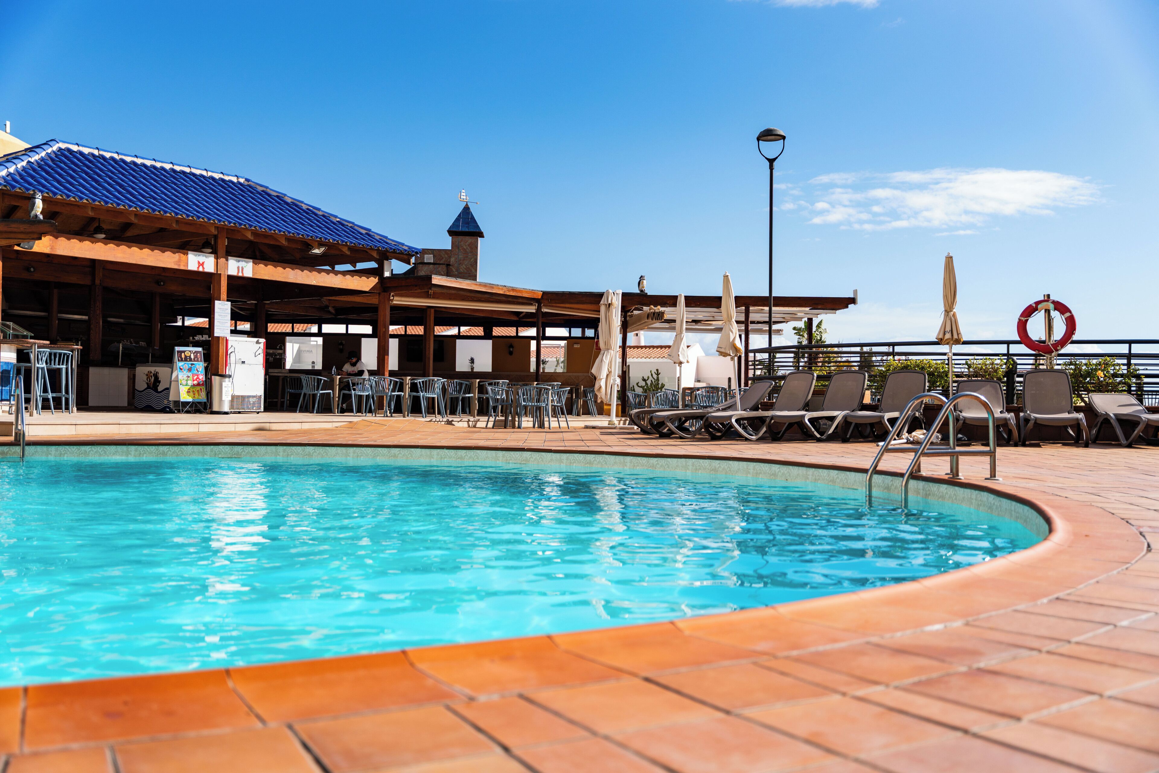 A pool area with a clear blue pool, sun loungers, and a covered seating area with umbrellas.