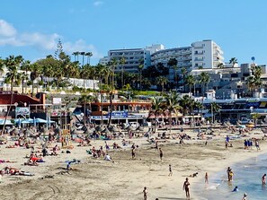 Ein Strand mit Menschen, Sonnenschirmen und Gebäuden im Hintergrund.