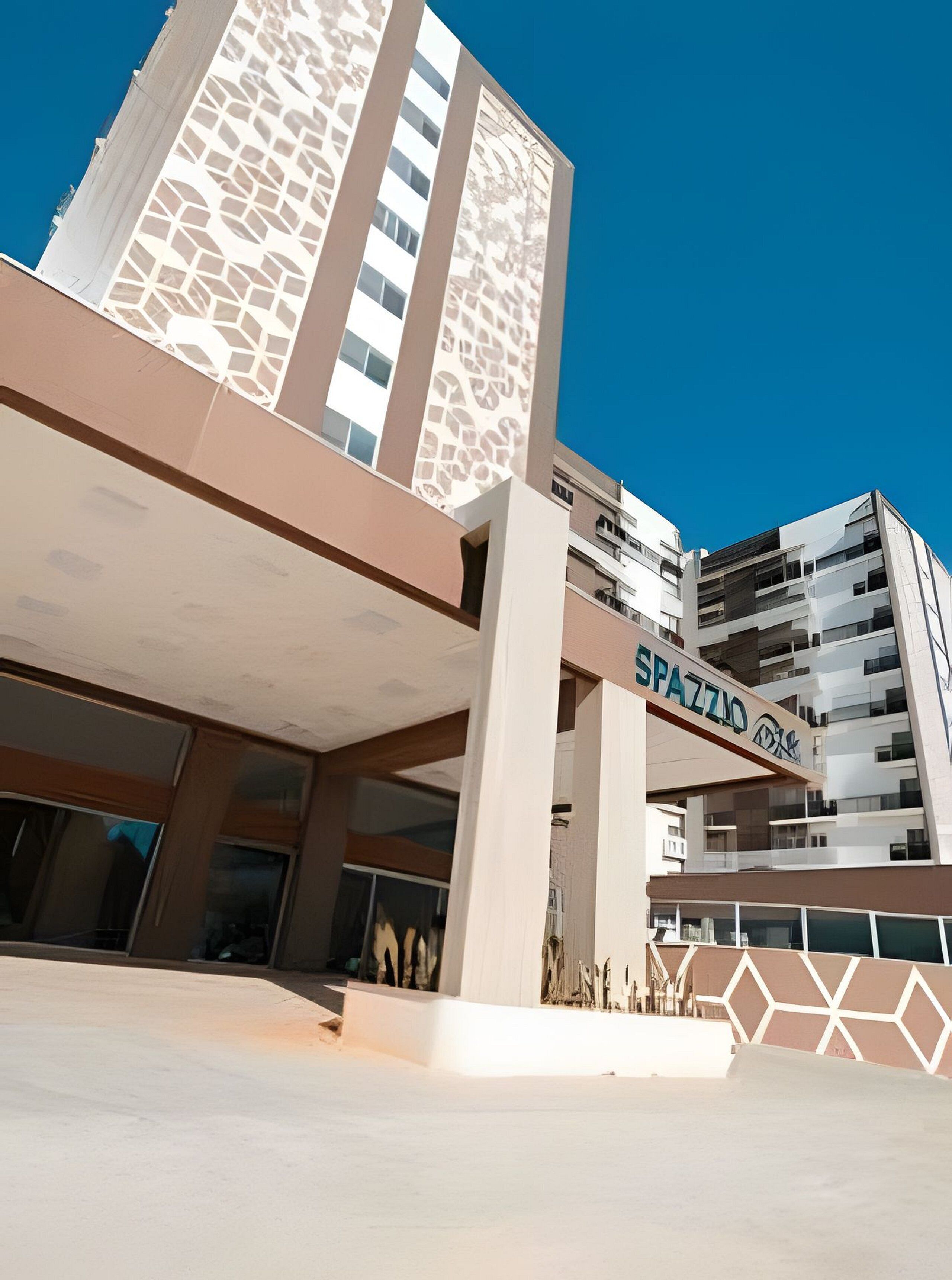Um edifício moderno com entrada destacada e uma placa com o texto 'SPAZZINO'.