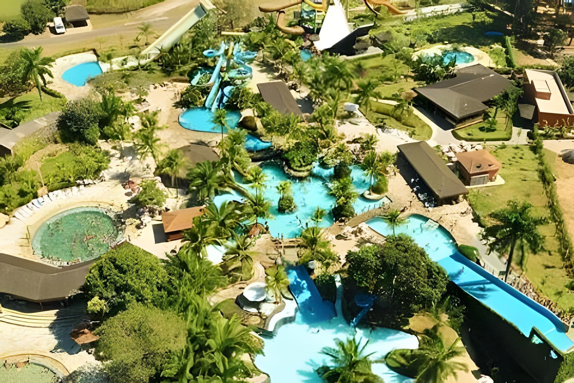 An aerial view of a resort with multiple swimming pools, palm trees, and a variety of buildings.