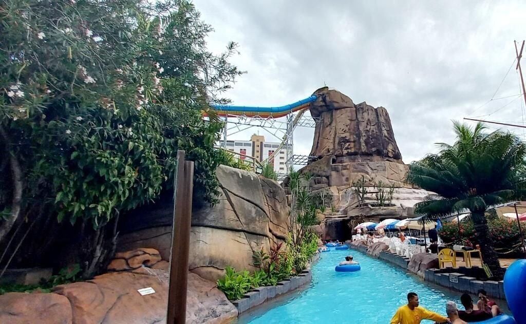 Ein Wasserpark mit einer großen Felsformation, einer Wasserrutsche und einem Poolbereich mit Liegestühlen.