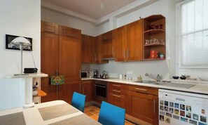 A compact kitchen with wooden cabinets, a microwave, a sink, and a dishwasher. - BRIGHT & ELEGANT 63M² PARISIAN RETREAT (Paris)