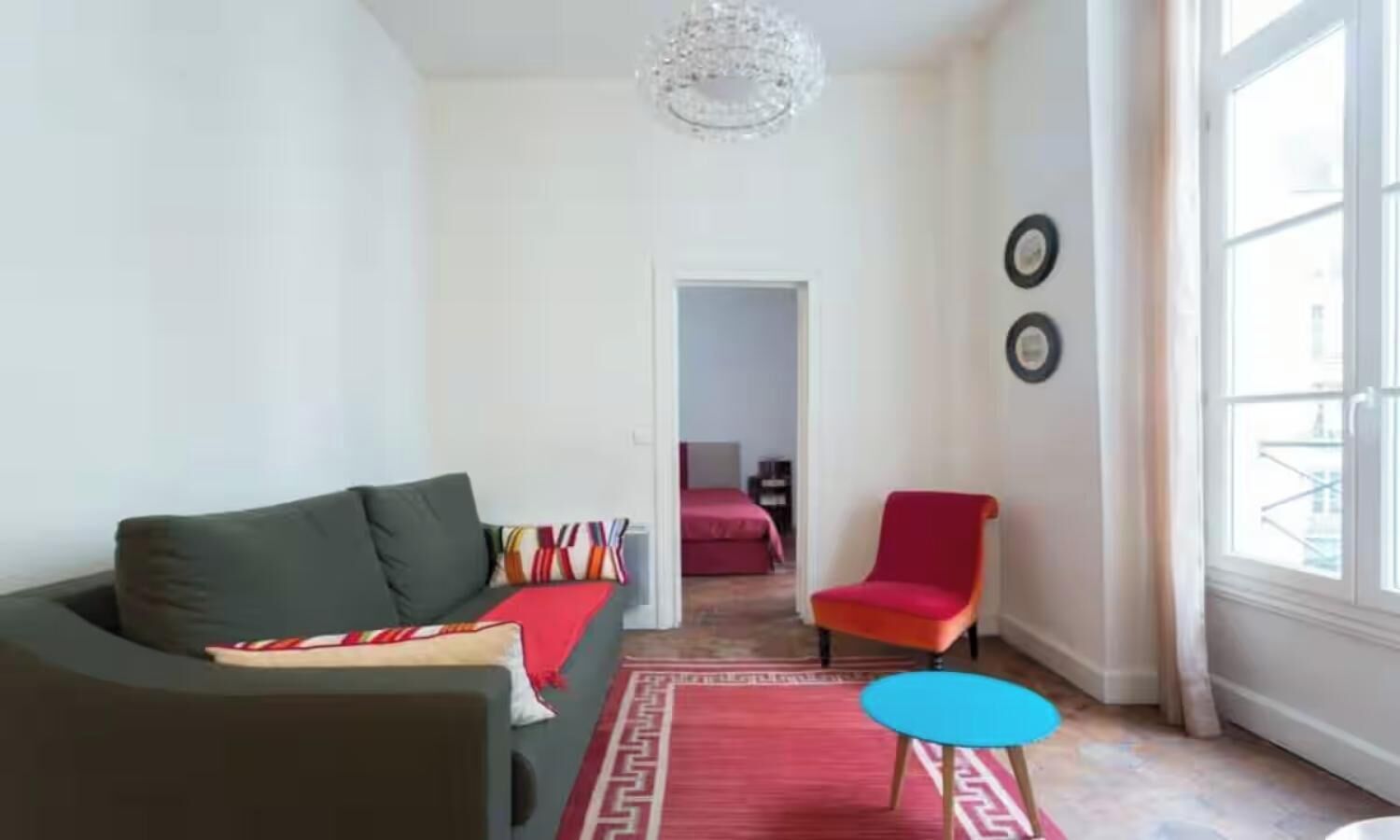 Ein Wohnzimmer mit einer Couch, einem roten Sessel, einem kleinen Tisch und einem gemusterten Teppich.