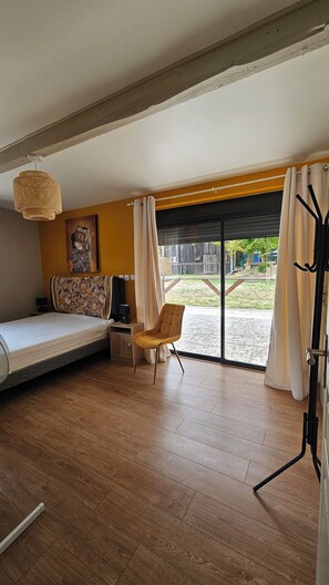 Een kamer met een bed, een stoel, een tafel, een lamp en een schilderij aan de muur.