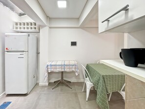 Una cocina compacta con un refrigerador blanco, una mesita con mantel a cuadros y una mesa cubierta con mantel verde.