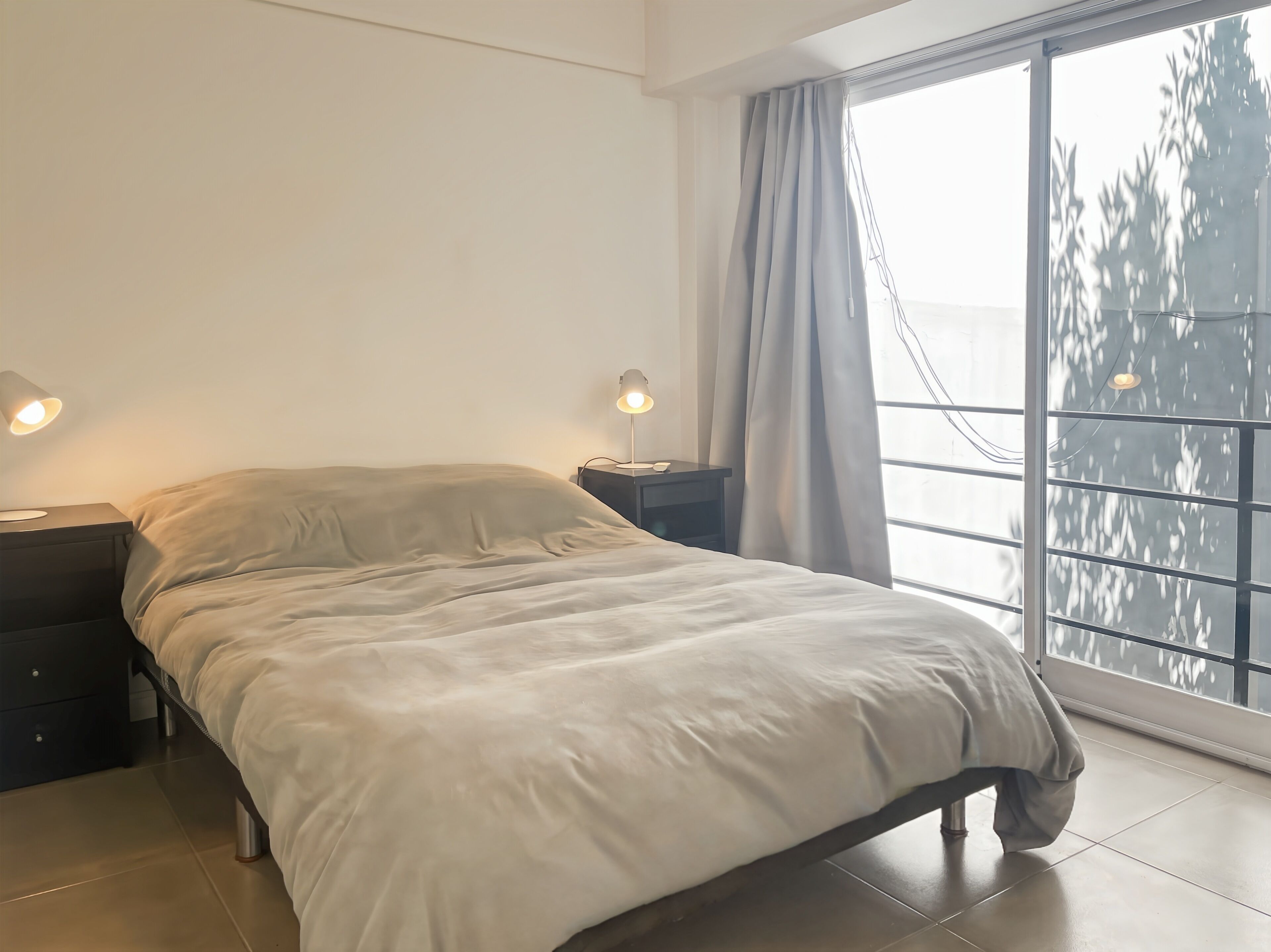 A bedroom with a bed, two bedside tables, a window with curtains, and a view of trees outside.